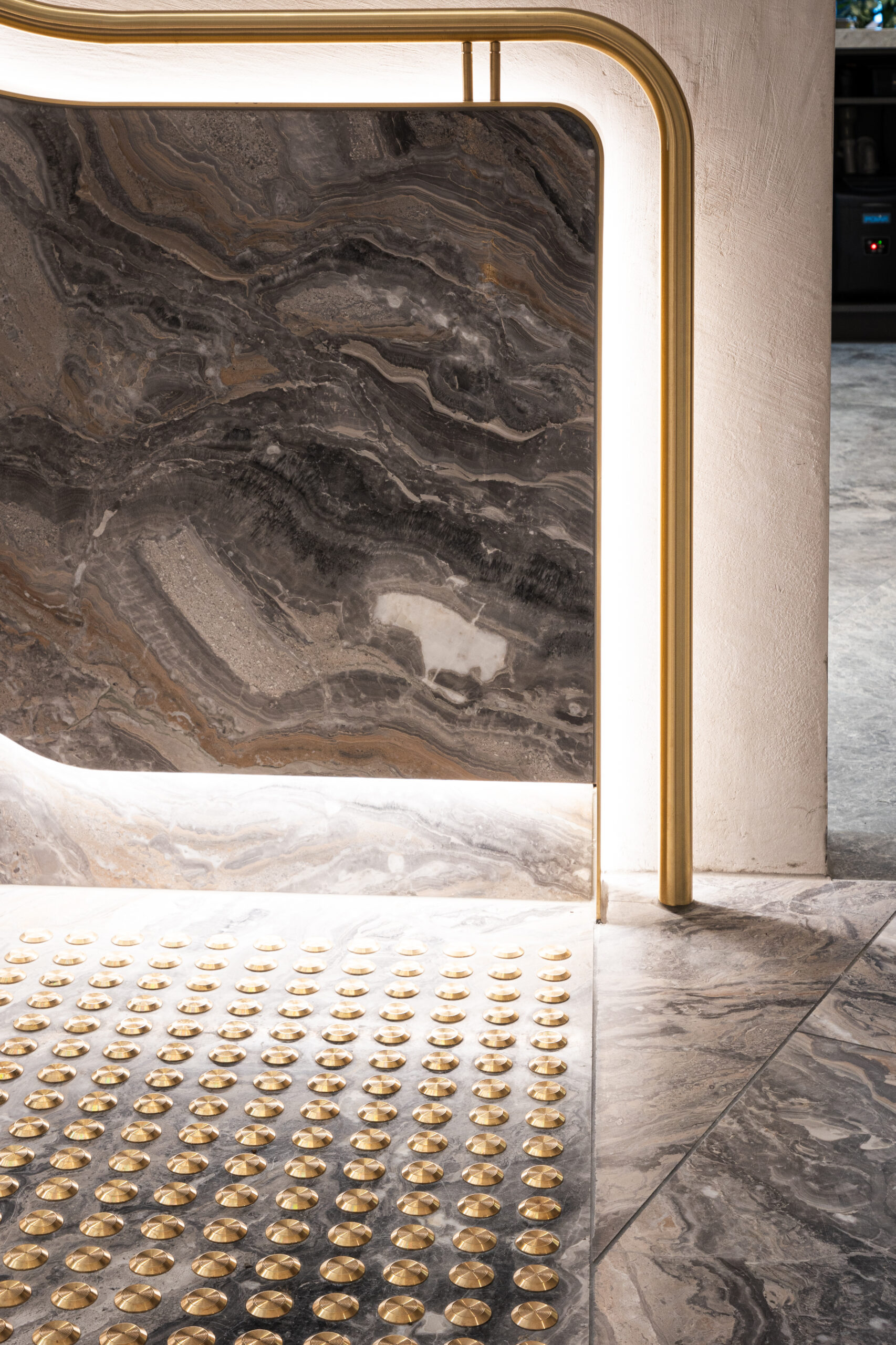 Elegant interior with a polished stone wall with swirling brown and gray patterns, surrounded by a brass frame and solid brass tactiles.