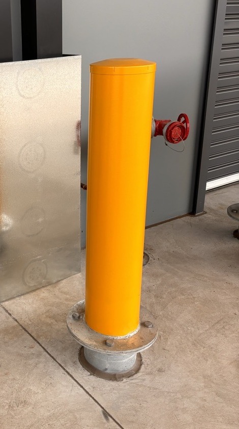 A yellow breakaway bollard mid-installation in an industrial property.