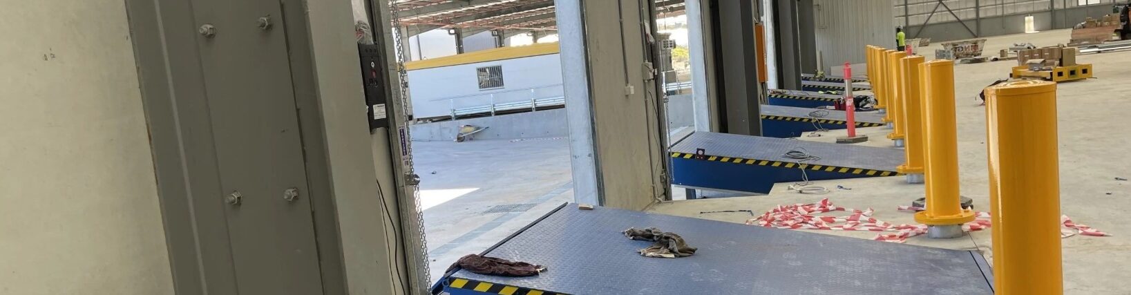 Yellow breakaway bollards installed next to loading dock ramps in a factory.