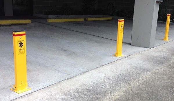 Collapsible bollards with a reflective sign installed in front of parking bays.