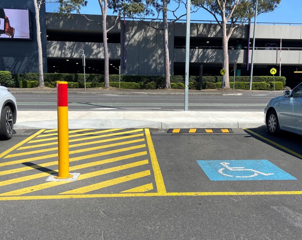 A disabled bollard installed next to a disabled parking bay in an outdoor car park.