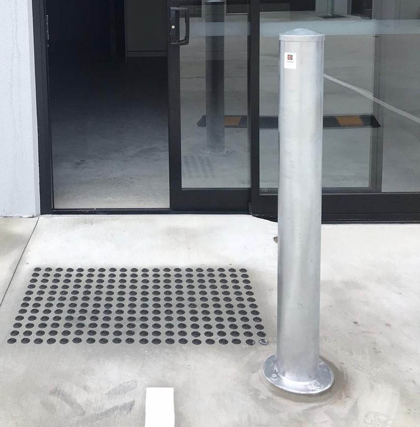 A galvanised steel bollard installed in front of a building entrance.