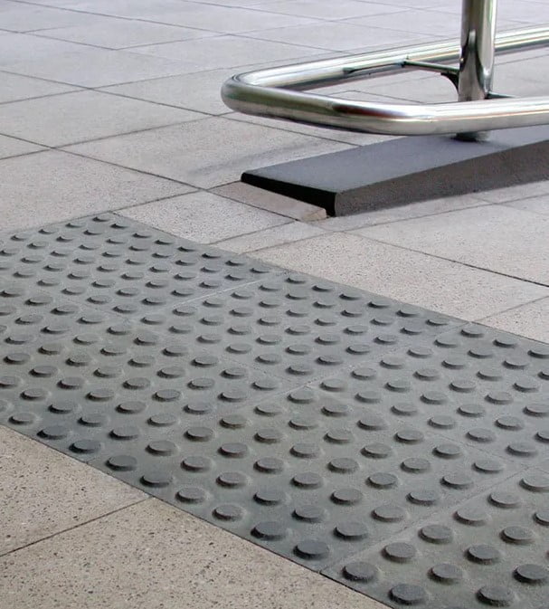 Concrete warning tactiles pavers on a tiled walkway is near a sleek, shiny metal railing.