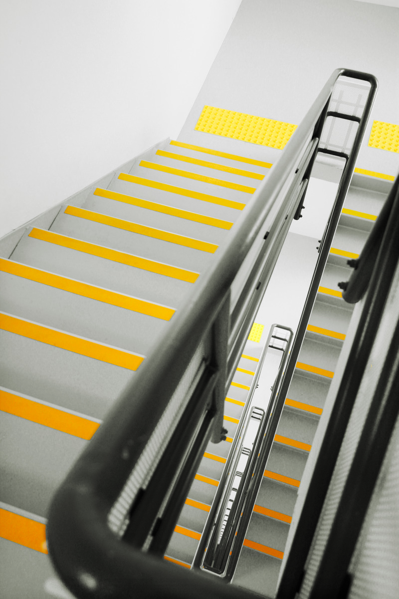 Looking down a modern staircase with gray steps and anti-slip yellow stair nosing tapes.