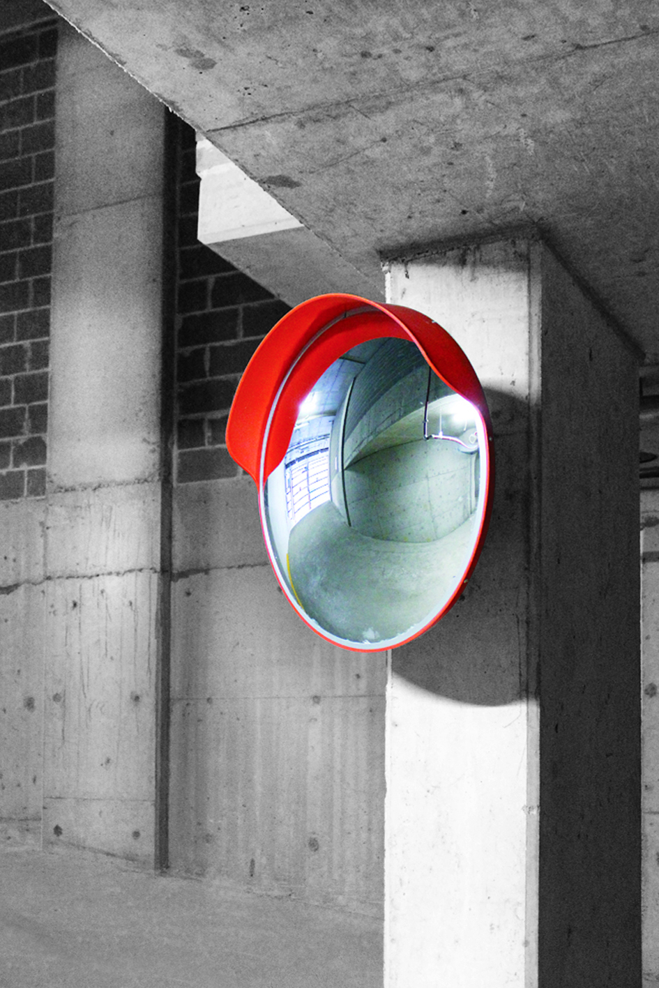 A convex car park safety mirror installed at a height on a concrete pillar.