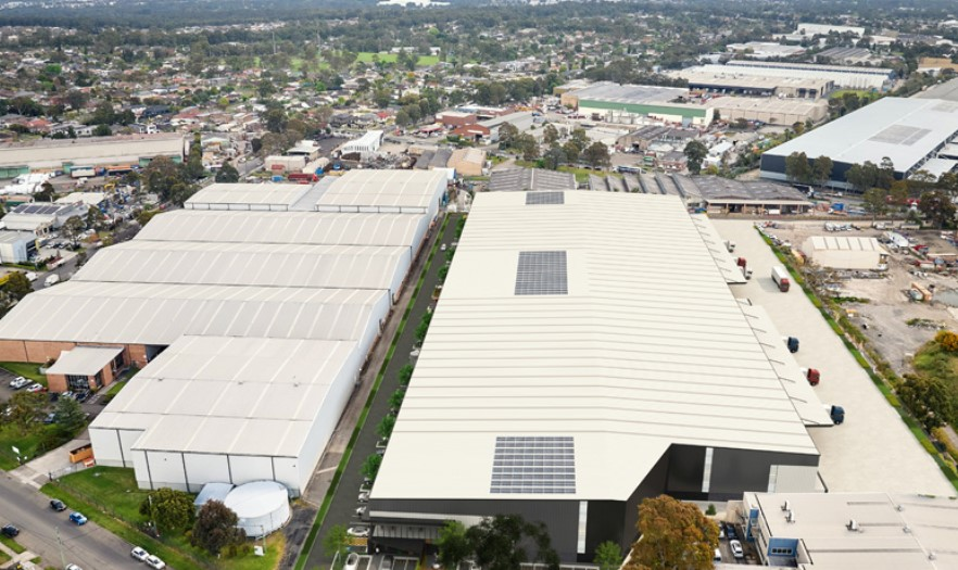 Aerial view of a large industrial complex with white warehouse roofs, surrounded by an urban neighbourhood.