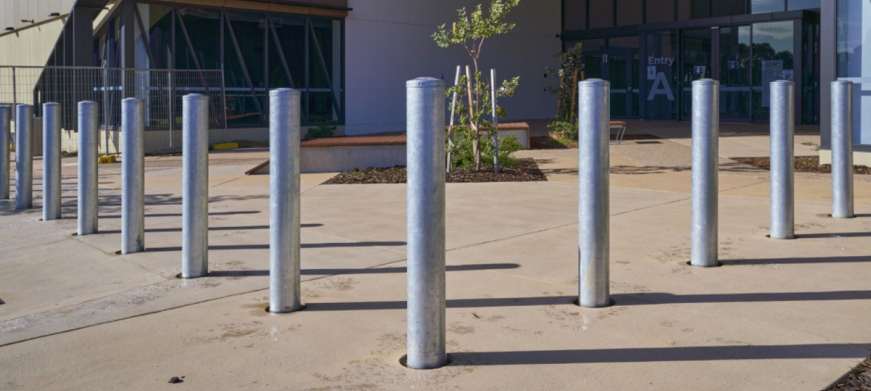 Rows of steel bollards line a concrete pathway leading to a building entrance.